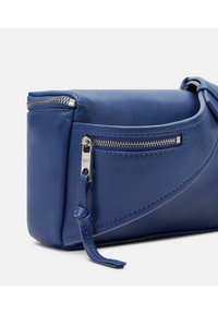 Borsa a mano in pelle blu con una tasca con zip, design elegante, texture liscia e un caratteristico dettaglio con cucitura curva. Accenti in metallo.