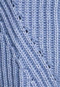 Světlomodrá pletená tkanina s texturovaným vzorem cik-cak, který obsahuje vystouplé stehy a otevřené prostory vytvářející vrstvený vzhled.