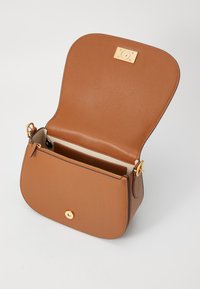 Borsa a tracolla in pelle marrone con forma curvata, accessori dorati, chiusura magnetica e una tasca interna con zip. Texture liscia, design minimal.