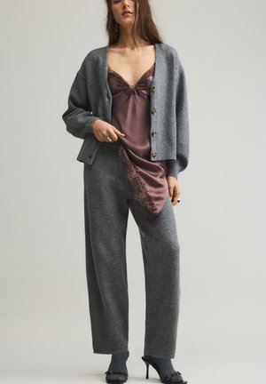 Grå strikket cardigan med store knapper, lagdelt over en bordeaux satin natkjole med blonder, kombineret med grå bukser med vide ben og sorte hæle.