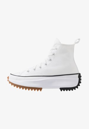 Sneaker alta bianca con tomaia in canvas, accenti in gomma nera e marrone, suola seghettata sorprendente e occhielli in argento con lacci.