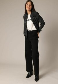 Zwarte bomberjack met witte spikkels over een witte graphic t-shirt. Gecombineerd met hoge zwarte broek en zwarte haklaarzen.