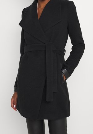 Schwarzer Wollmischmantel mit doppelreihigem Design, breiten Revers, tailliertem Gürtel und Lederakzenten an den Manschetten. Glatte Textur, mittellange Passform.