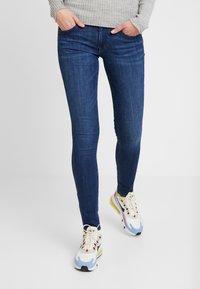 Jeans de denim azul ajustados con una textura suave y diseño clásico de cinco bolsillos, combinados con zapatillas multicolores con detalles de cordones.