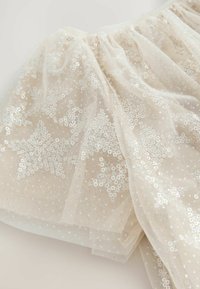 Jupe en tulle beige clair ornée de sequins en forme d'étoile argentés, avec une ceinture froncée et une texture douce, mettant en valeur des détails raffinés sur le tissu.