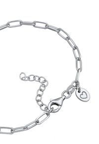 Silverfärgad kedjebröst med avlånga länkar, en hummerlås och en liten hjärtformad charm med ett ingraverat hjärtformat mönster.