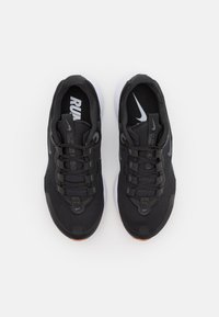 Zapatillas deportivas negras que cuentan con una parte superior de malla, cierre de cordones y suela blanca. Detalles notables incluyen un logo en la lengüeta y acentos texturizados.