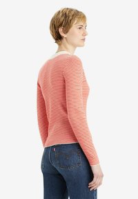 Langärmliges Oberteil mit rot-weißen Streifen und rundem Halsausschnitt, kombiniert mit dunkelblauen Jeans aus Denim mit genähten Gesäßtaschen.