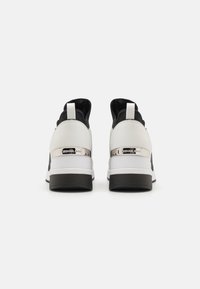 Sneaker bianche e nere con tomaia in pelle liscia e mesh, caratterizzate da un accento argento nel tallone e una suola in gomma nera testurizzata.
