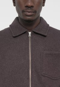 Dark gray fleece jacket, with a zip closure, pointed collar, and a single chest pocket. Soft texture with minimal detailing.