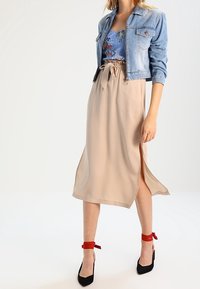 Light blue denim jacket over a floral-printed tank top, paired with a beige midi skirt featuring a side slit. Black heels with red ankle ties.