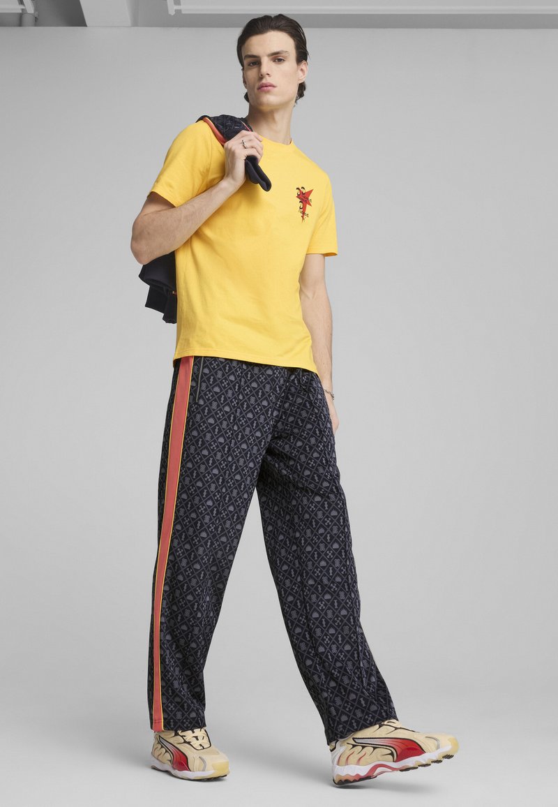 T-shirt en coton jaune avec un design graphique rouge, associé à un pantalon large à motifs marine avec des rayures rouges et jaunes. Baskets en beige et rouge.