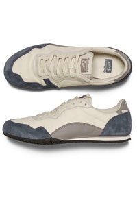 Kremowo-szare zamszowe trampki z gładką skórzaną cholewką, okrągłym noskiem, płaską gumową podeszwą i sznurowanym zapięciem. Czarna podeszwa z teksturowanym wzorem.