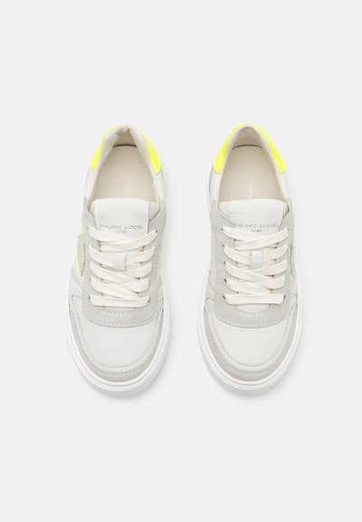 Weiße und hellgraue Sneakers mit einem Obermaterial aus Wildleder und Leder, runder Zehenpartie und neon gelben Akzenten, flachen Schnürsenkeln und einer strukturierten Sohle.