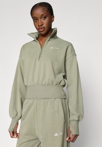 Απαλή πράσινη, φερμουάρ, πουκαμίσα με στάμπα και μανίκια με ραφή. Διαθέτει διακριτική λεπτομέρεια λογότυπου σε λευκό χρώμα. Με απαλή υφή υφάσματος.