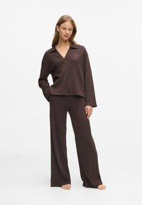 Rjav, rebrast material loungewear set, ki vključuje majico s ovratnikom in dolgimi rokavi ter široke hlače s sproščenim krojem in subtilnim logotipom.