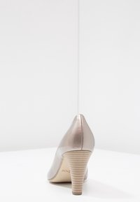 Béžové lakované lodičky na vysokém podpatku se špičatou špičkou, s texturovaným světlým sloupcovým podpatkem. Hladký povrch a elegantní design.