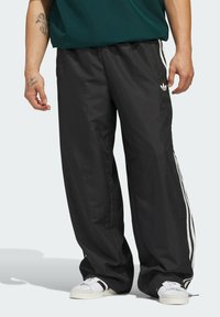 Čierne športové nohavice z ľahkého a priedušného materiálu. Majú biele bočné pruhy a vyšívané logo, uvoľnený strih a elastický pás.