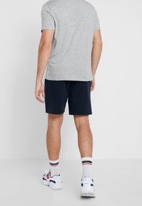Grå t-shirt med kort ärm som matchas med marinblå shorts, vita strumpor med röda och blå ränder och sportskor med röda detaljer.