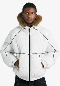 Biela prešívaná bunda s čiernym pre�šívaním, kapucňou lemovanou kožušinou a elastickými manžetami. Má zipsové zapínanie a boxovitý strih.