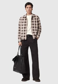 Γκρι καρό πουκάμισο με κουμπιά πάνω από λευκό τοπ, σετ με μαύρο παντελόνι και μαύρη δερμάτινη τσάντα tote. Μαύρα παπούτσια με ανοιχτές σόλες.