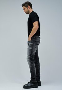 Camiseta negra combinada con jeans ajustados grises, con un lavado desvanecido y un leve desgaste. Botines negros completan el conjunto.