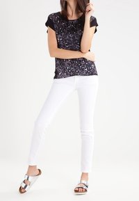 Top corto de leopardo en negro y gris, combinado con jeans ajustados blancos y sandalias de deslizar plateadas con doble hebilla.