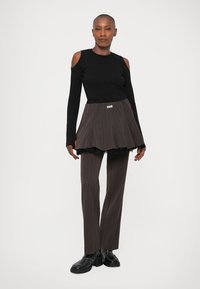 Pull noir à manches longues avec épaules dégagées, associé à une jupe marron à rayures et un pantalon assorti. Des chaussures noires brillantes complètent le look.