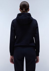 Sudadera marina con una textura suave y una capucha grande, con puños y dobladillo acanalados. Combinada con pantalones marinos a juego, mostrada desde la parte de atrás.