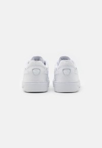 Paire de baskets blanches vues de dos, présentant un design épuré avec un logo discret sur la languette du talon, sur un fond uni.
