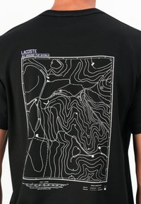T-shirt noir avec un imprimé de carte topographique blanche au dos, présentant des lignes de contour ainsi que des classifications routières détaillées et du texte d'échelle.