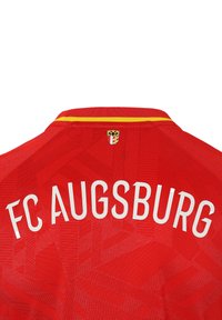 Maillot de football rouge avec "FC AUGSBURG" imprimé en blanc au dos. Présente un design texturé et un col rayé jaune et rouge.