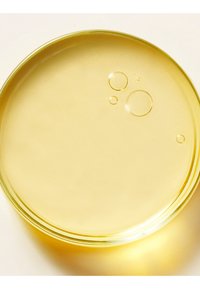 Klar gul væske med nogle få bobler inde i en rund transparent glasfad på en hvid baggrund.