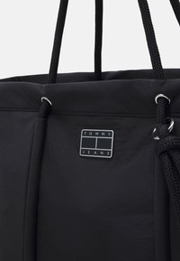Svart Tommy Jeans tote-väska med tjocka flätade handtag och en liten rektangulär logotags på framsidan.