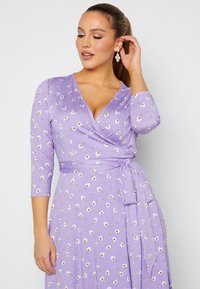 Lila Wickelkleid mit Dreiviertelärmeln, das ein florales Muster aus weißen Margeriten und Grün aufweist. Weicher, glatter Stoff mit einem taillierten Detail.