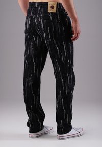 Black jeans with a textured pattern featuring white streaks. Back view shows a leather patch and five-pocket design, paired with white sneakers.
