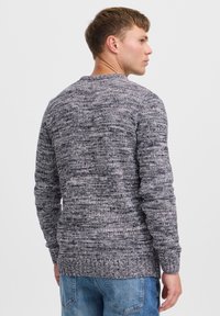 Gray knit sweater with varied texture. Round neckline, long sleeves, and ribbed cuffs. Worn over light blue jeans.
