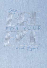 Tela de color azul claro con texto bordado: "Fresca BRISA PARA TU mente y alma EZE", que presenta una mezcla de líneas gruesas y finas en plata y verde azulado.