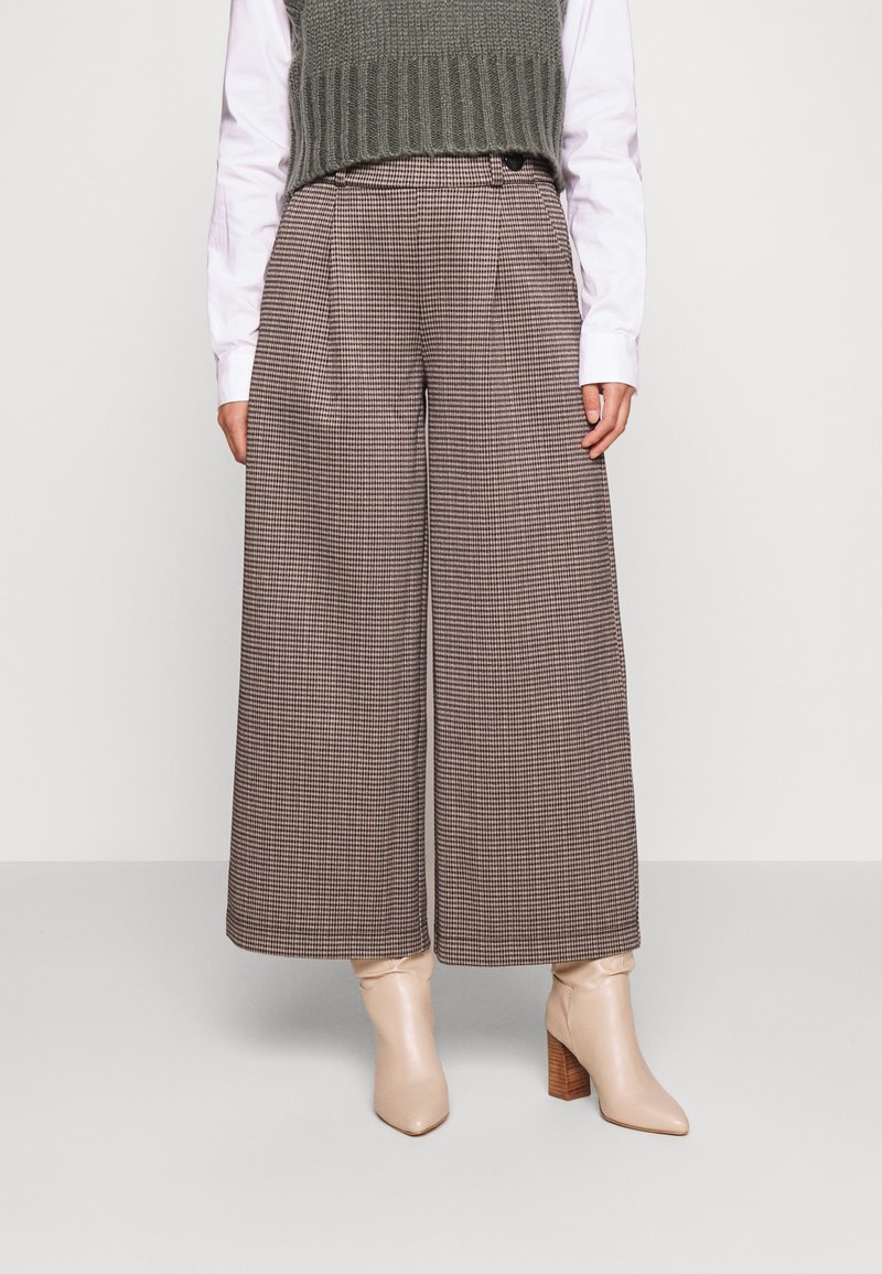 Vida byxor i brunt rutmönster, med hög midja och lös passform. Kombinerat med en grön stickad väst och beige klackiga ankelskor.