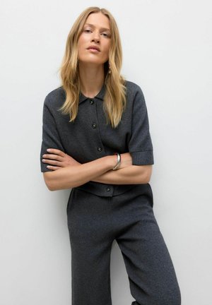 Haut en tricot mélange de laine gris foncé avec des manches courtes, fermeture à boutons et poignets côtelés, associé à un pantalon large assorti.