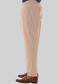 Pantaloni beige su misura con elastico in vita, tasche laterali e una texture liscia, abbinati a mocassini intrecciati marroni.