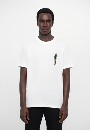 White cotton t-shirt featuring a small graphic print on the chest. Short sleeves, round neckline, relaxed fit. Black pants worn below.