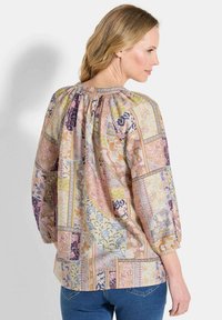 Bedruckte Bluse in Pastellfarben mit gerafftem Ausschnitt, langen Puffärmeln und einer Mischung aus floralen und geometrischen Mustern.