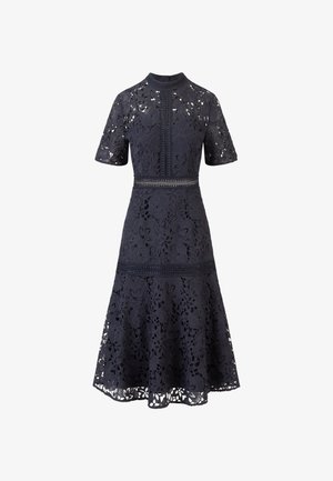 Tummansininen pitsimekko, jossa on kukkakuosi, lyhyet hihat, korkea kaula-aukko ja tiukka vyötärö. Levittäytyvä hame, jossa on koristeellisia trimmaus yksityiskohtia.