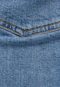 Tela de mezclilla en azul claro con una textura ligeramente desgastada, presenta costuras amarillas contrastantes a lo largo de una costura.