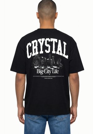Homme portant un T-shirt noir avec texte blanc « CRYSTAL » et un graphisme de silhouette de ville au-dessus du slogan « Big City Life » dans le dos.