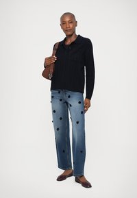 Marineblå strikkegenser med krage, kombinert med denimjeans med svarte blomsterapplikasjoner, og brun skulderveske. Maroon leiligheter fullfører antrekket.