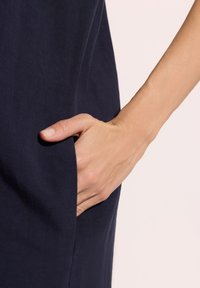 Granatowa odzież z boczną kieszenią, o gładkiej teksturze. Ręka jest włożona do kieszeni, ukazując naturalny odcień skóry.