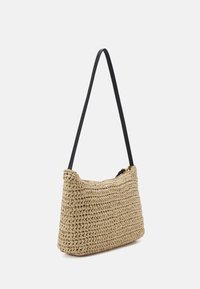 Tkaná slaměná taška přes rameno s jemným, zakřiveným tvarem, krémovou barvou, černým popruhem a zlatými akcenty u zipu.