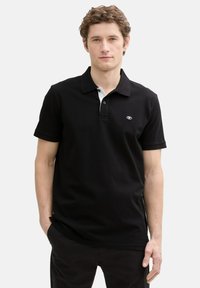 Svart polo skjorta med en texturerad tyg, kontrasterande vit krage och logotyp på vänster bröst. Korta ärmar och standard passform.